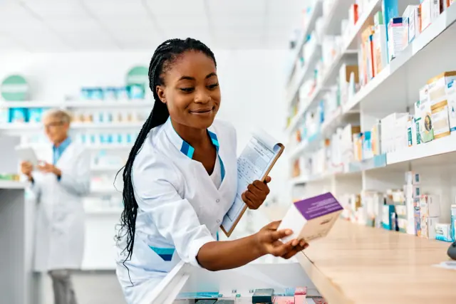 Une pharmacienne en blouse blanche prend une boîte dans un rayon de l’officine.
